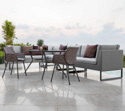 Modern outdoor seating arrangement with a grey sectional sofa, stylish chairs, and a glass-top table, adorned with decorative pillows.