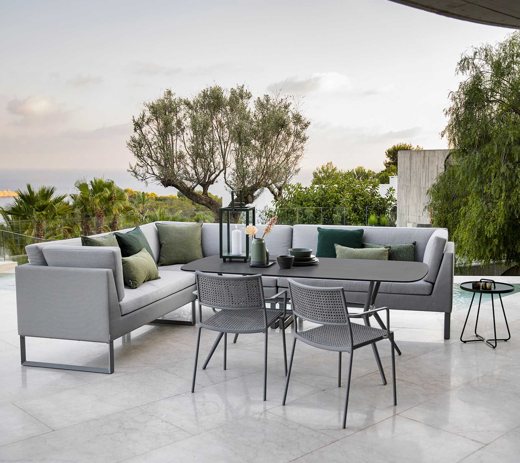 Modern outdoor seating area featuring a stylish sectional sofa, a dining table, and metal chairs surrounded by greenery.
