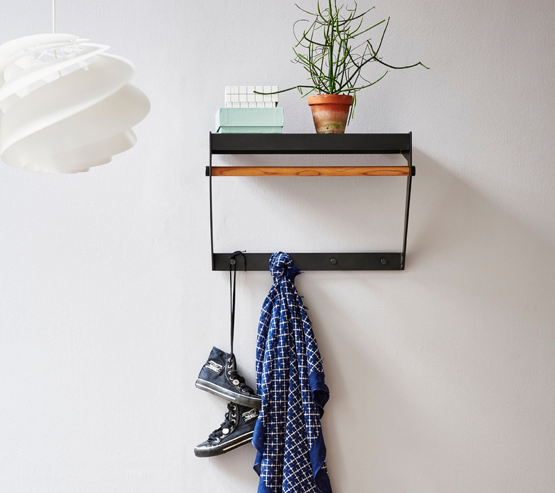 Wall-mounted shelf with a wooden top, featuring a small plant, a scarf hanging below, and a pair of shoes on the floor.