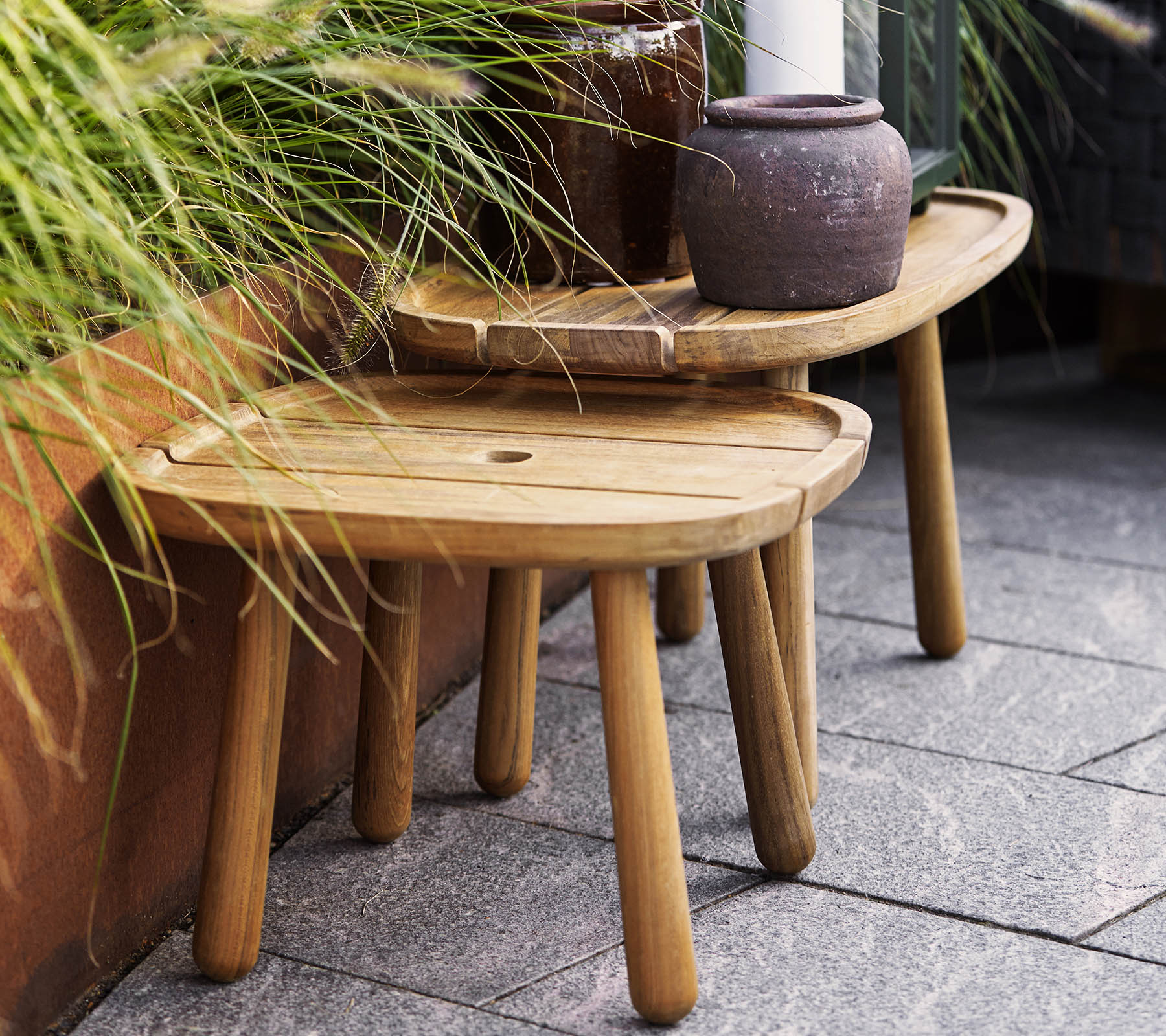 Two stylish wooden stools in varying heights, complemented by a ceramic pot and greenery in the background. Ideal for decorative use.