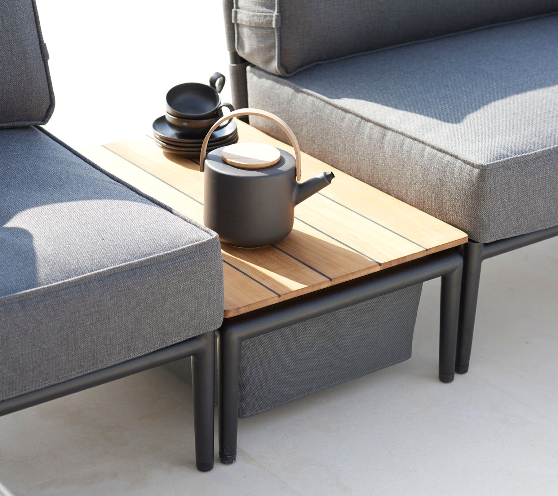 Two gray sofas flanking a wooden side table, topped with a black teapot and several cups, creating a cozy seating area.