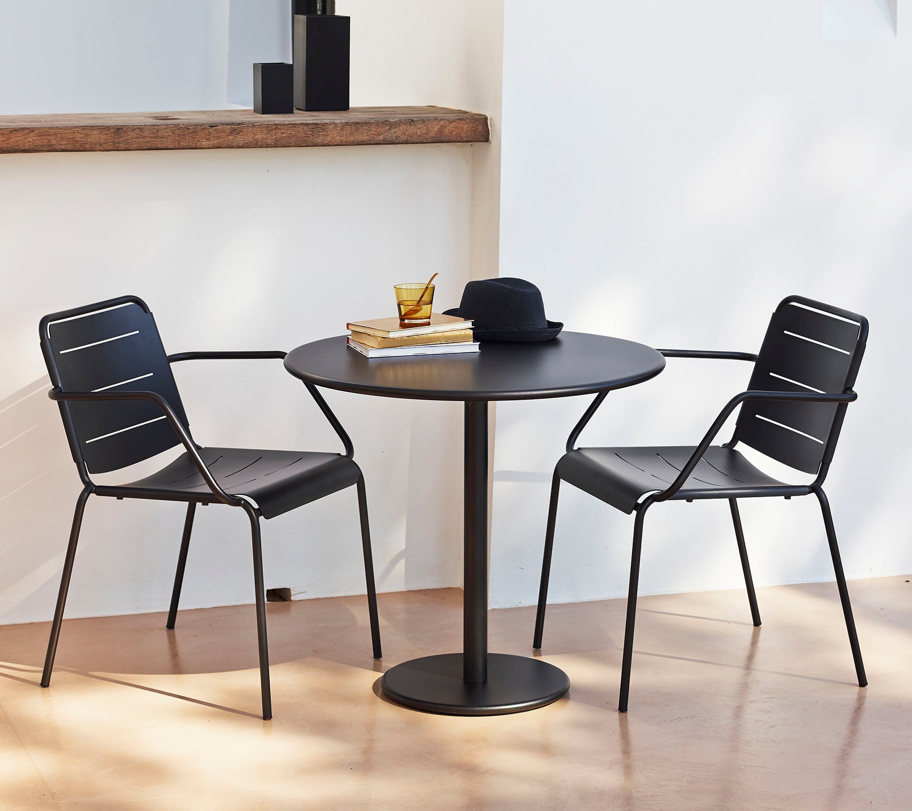A round table with two black chairs, topped with a hat and books, creating a stylish and inviting seating area.