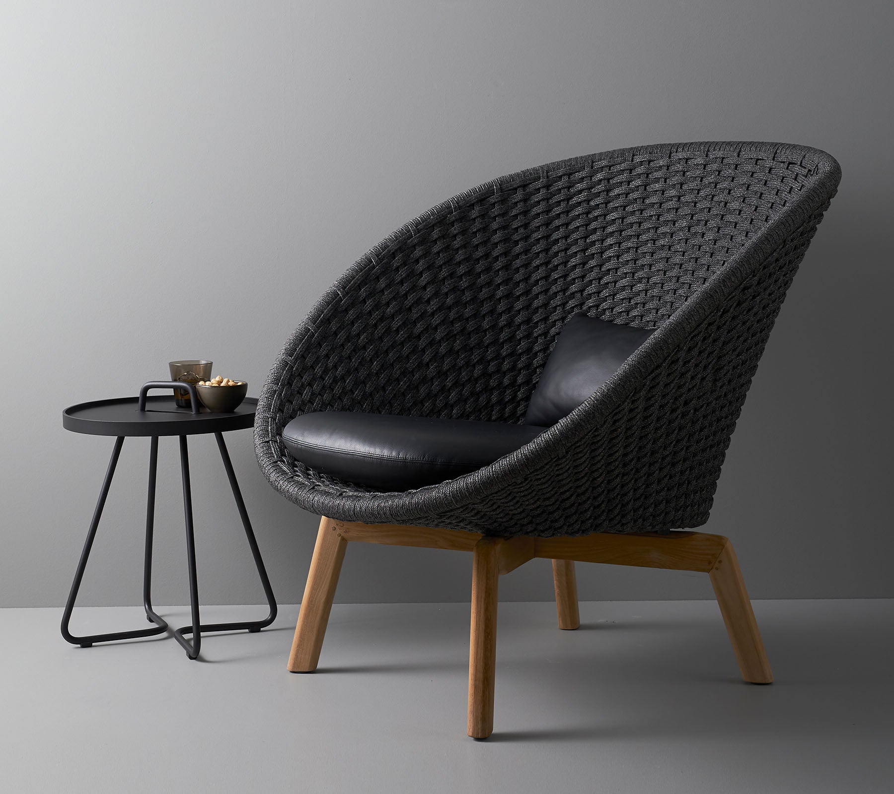 Stylish woven chair with a black cushion and a modern round side table, ideal for contemporary living spaces.