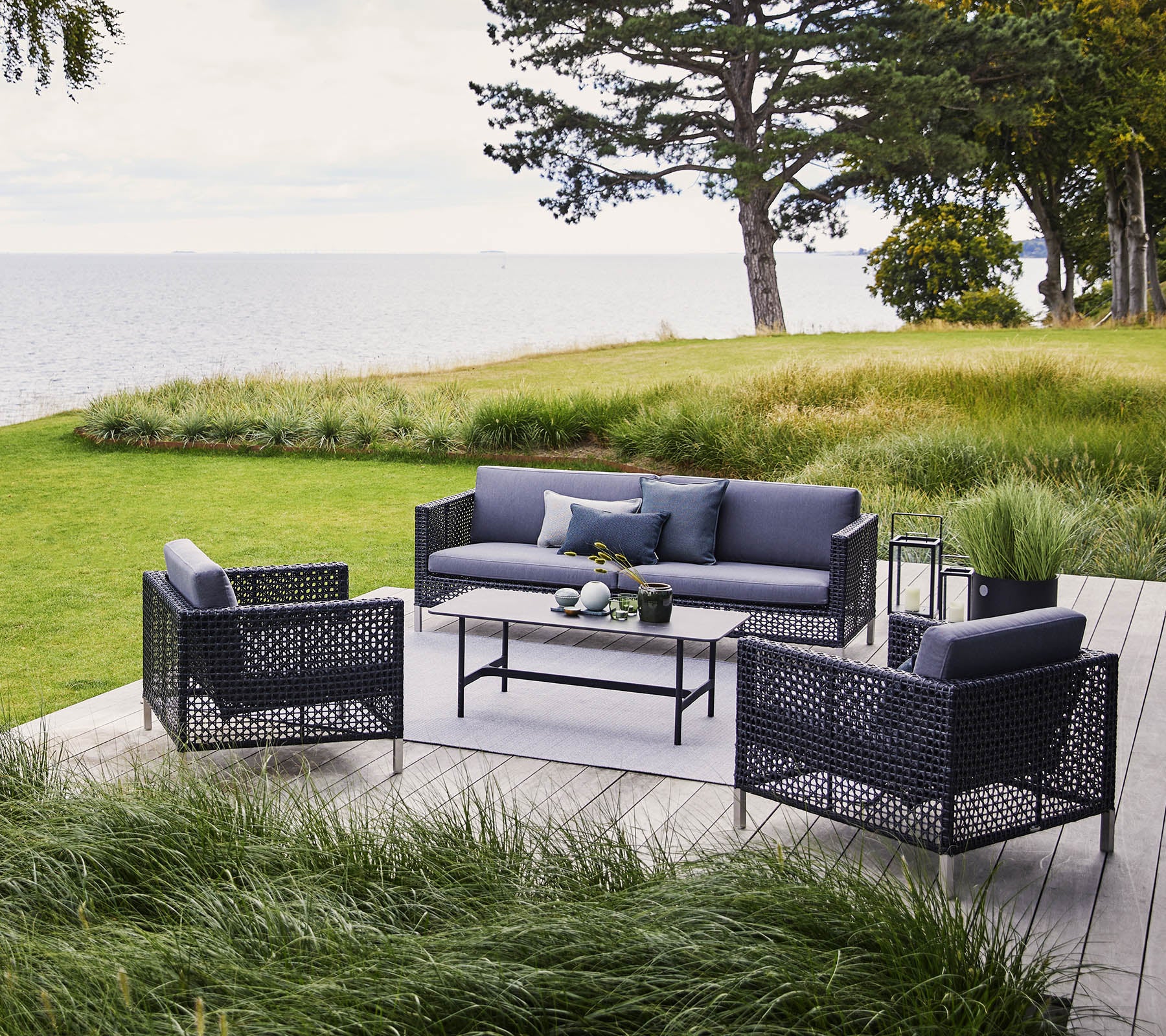 A stylish outdoor seating area featuring a sofa and two armchairs with dark wicker frames and comfortable cushions, accompanied by a coffee table.