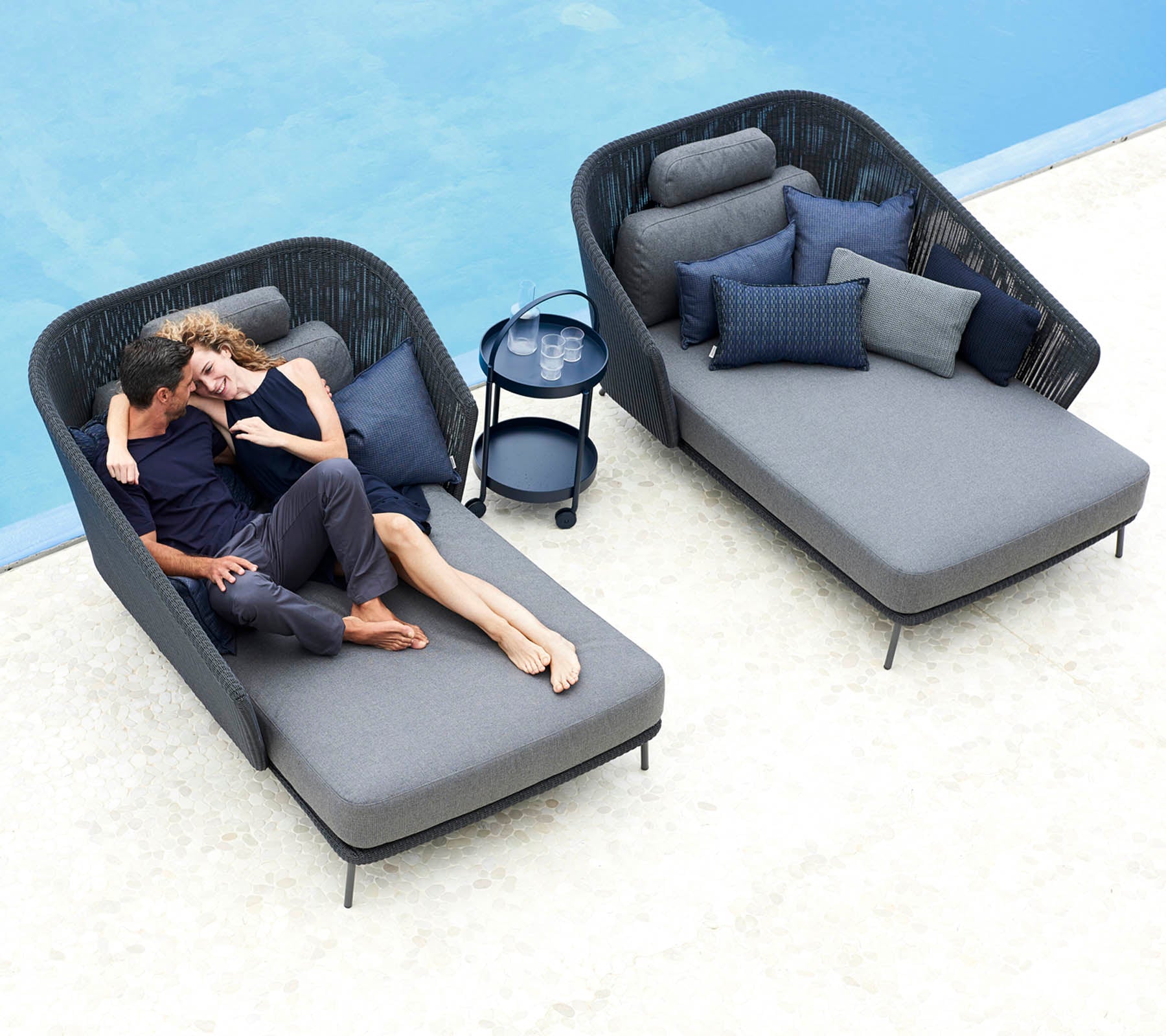 A couple relaxes together on stylish lounge chairs with plush cushions, accompanied by a small side table and decorative pillows.