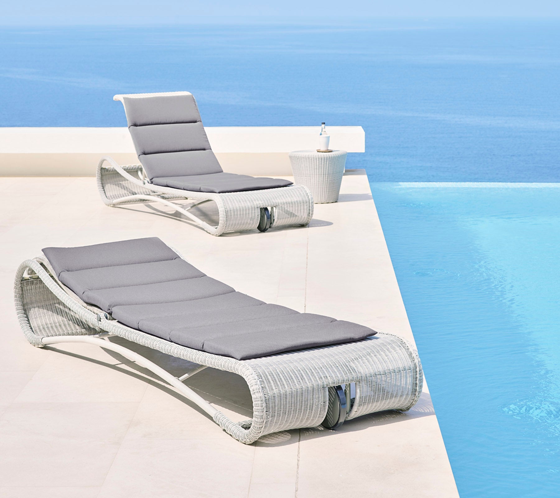 Two stylish lounge chairs with gray cushions beside a serene blue infinity pool, creating a relaxing outdoor space.