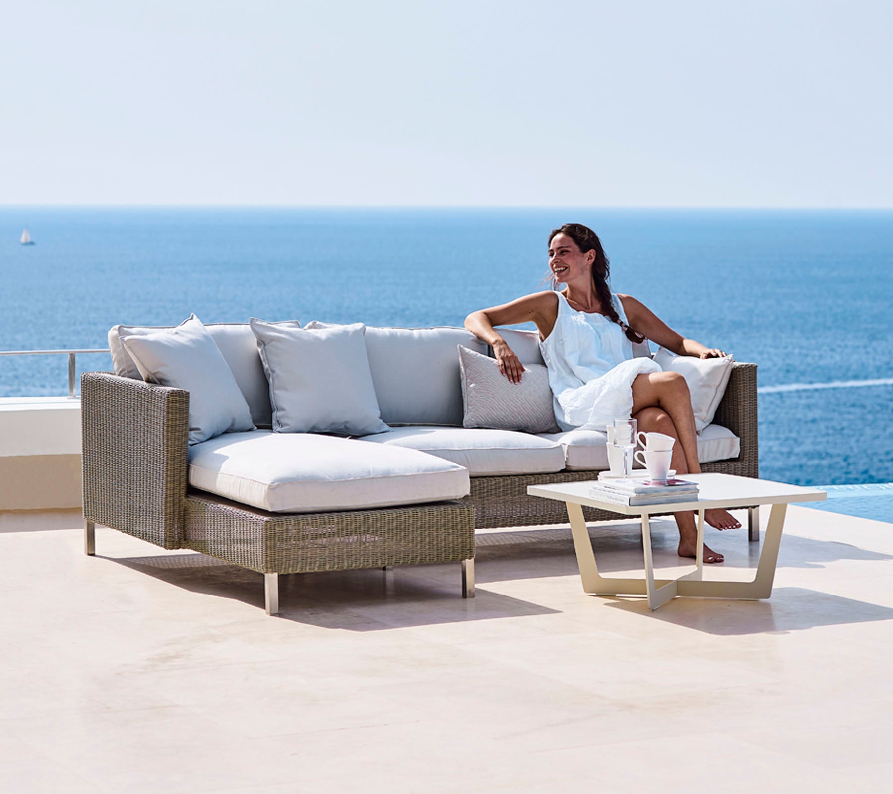 A woman lounging on a stylish sofa with plush cushions and a small table, overlooking a serene ocean view.
