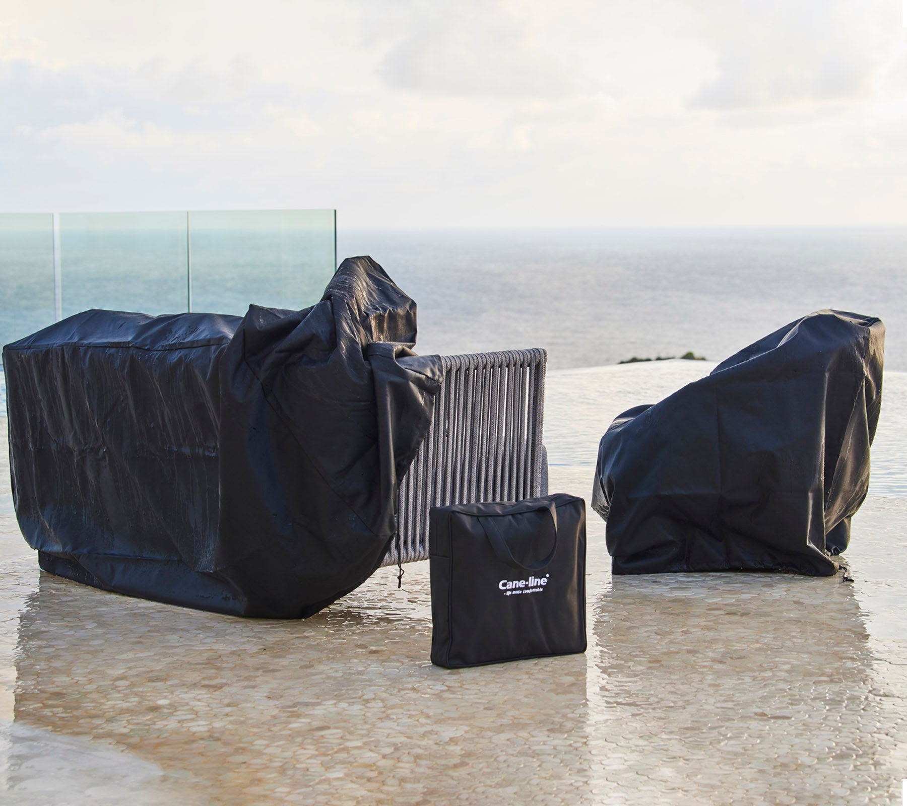 Outdoor furniture covers in black, protecting various pieces from weather elements, with one cover neatly folded nearby.