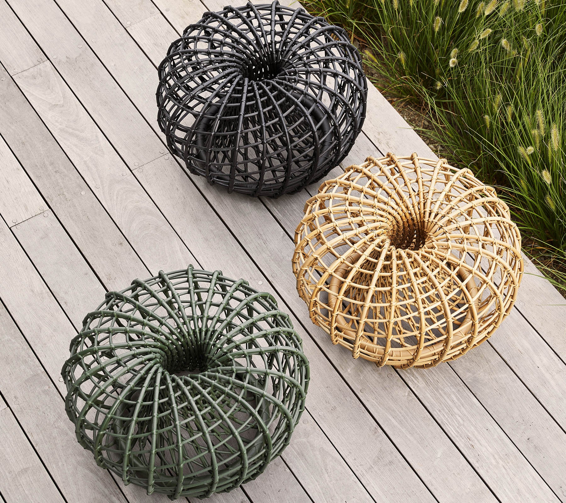 Three woven decorative baskets in black, green, and natural tones, arranged in a circular pattern on a wooden surface.
