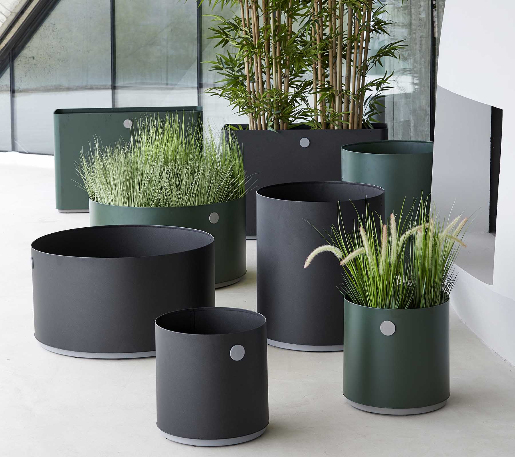 Various modern planters in dark tones, featuring ornamental grasses and plants, arranged in a stylish setting.