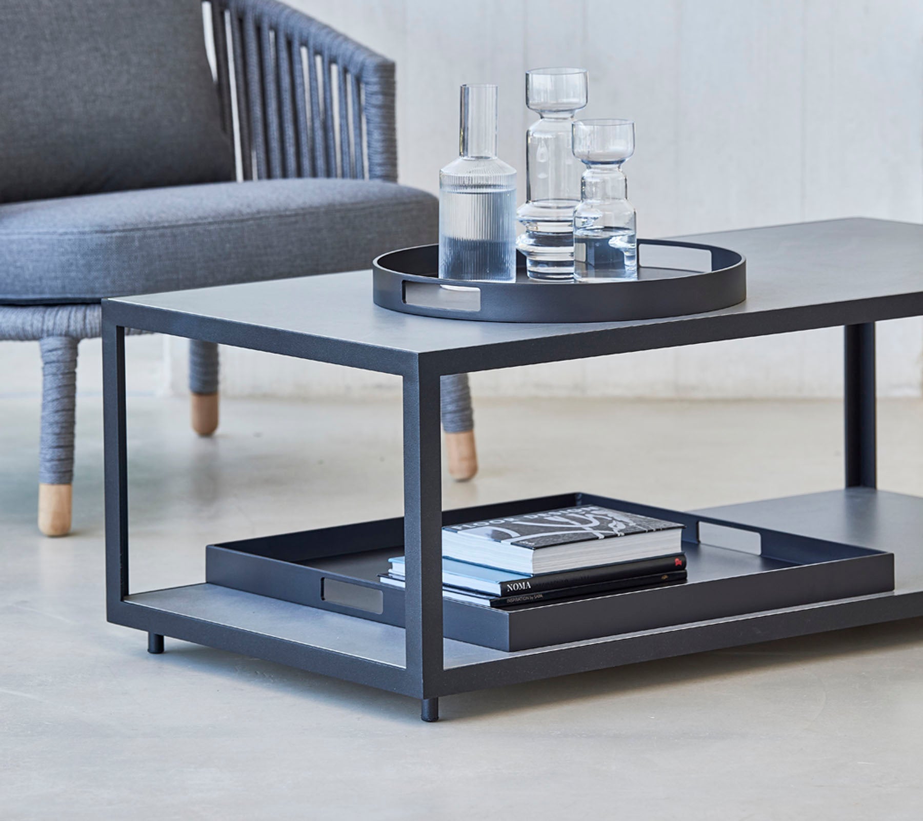 Modern coffee table featuring a sleek design, with a tray, glasses, and books on the lower shelf. Ideal for stylish living spaces.