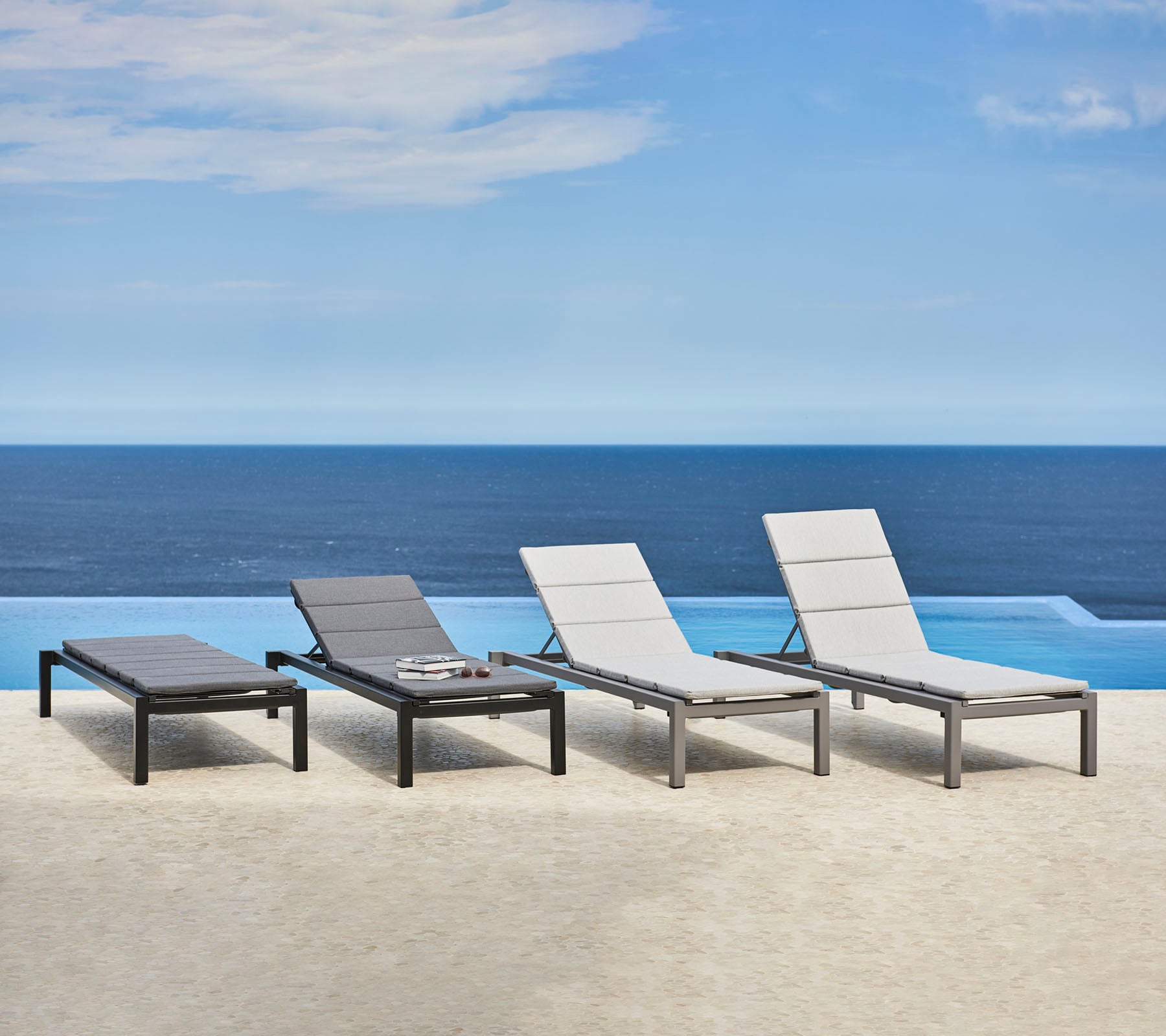Four stylish lounge chairs with a sleek design positioned near a serene body of water, creating a tranquil relaxation space.