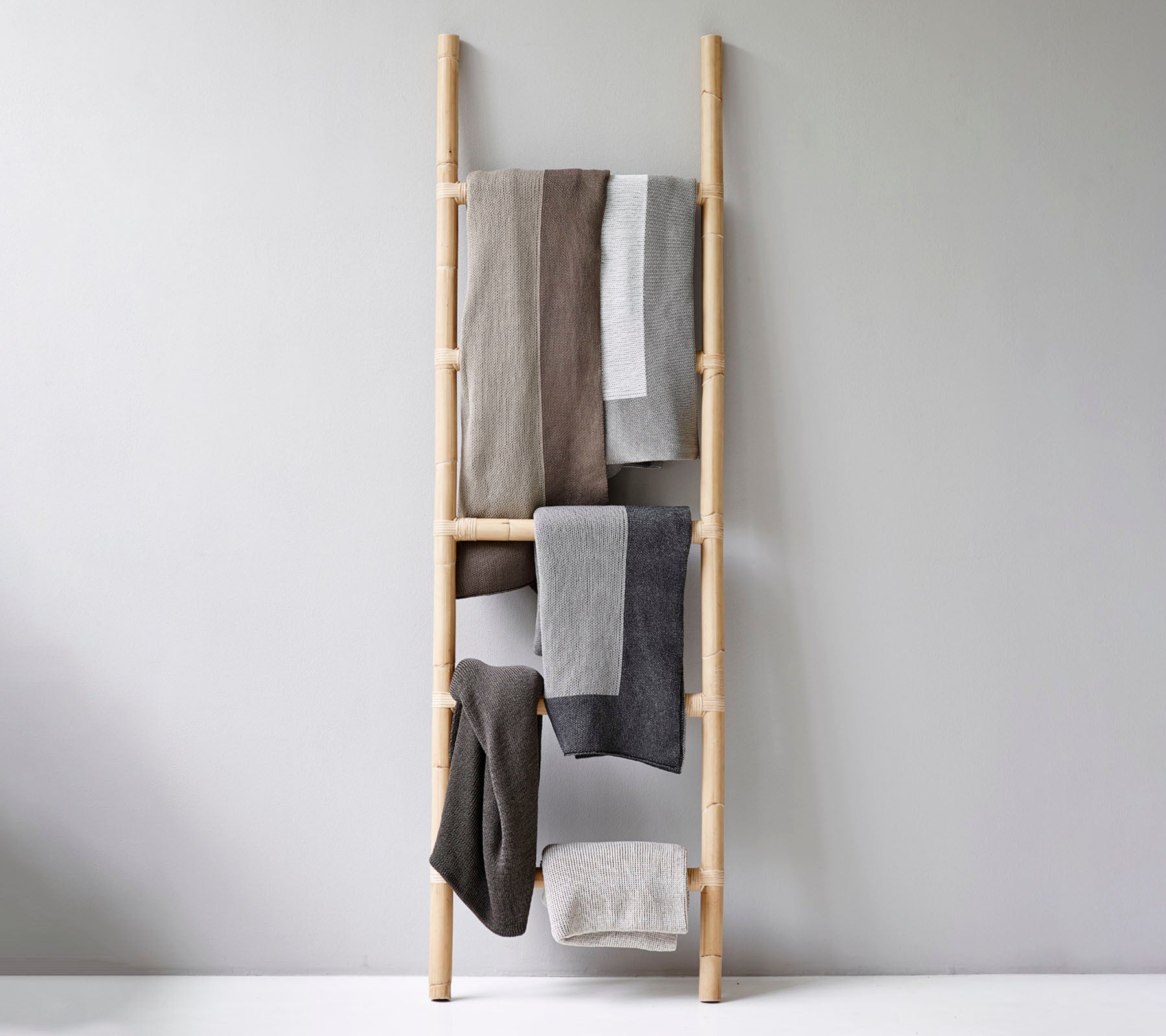 A wooden ladder displaying a variety of folded towels in neutral tones, arranged orderly for aesthetic appeal.