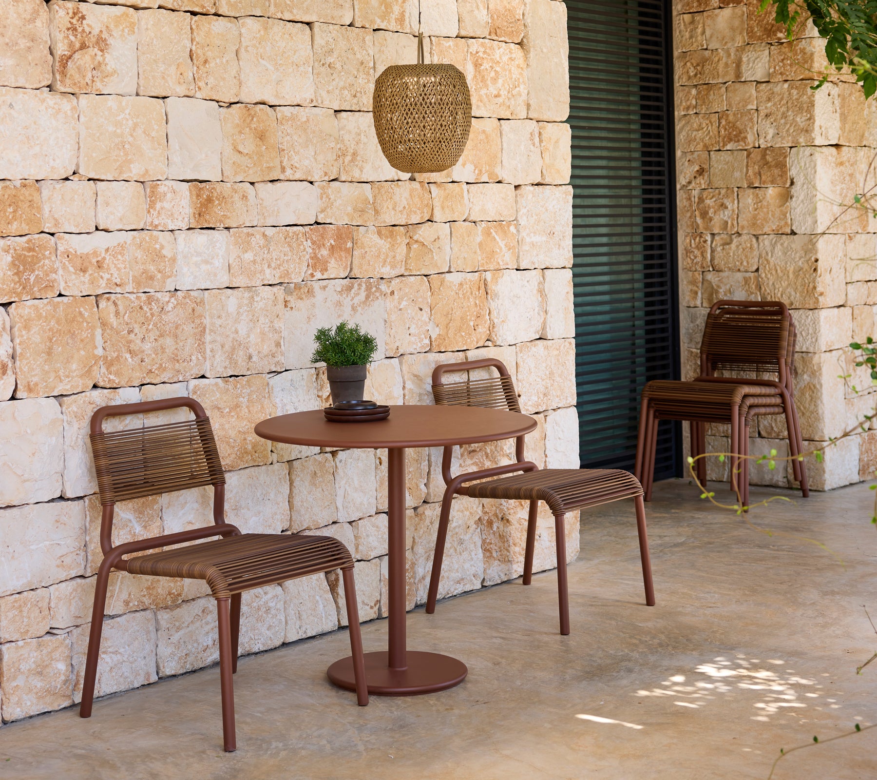 Modern outdoor seating with brown chairs and table against a stone wall.