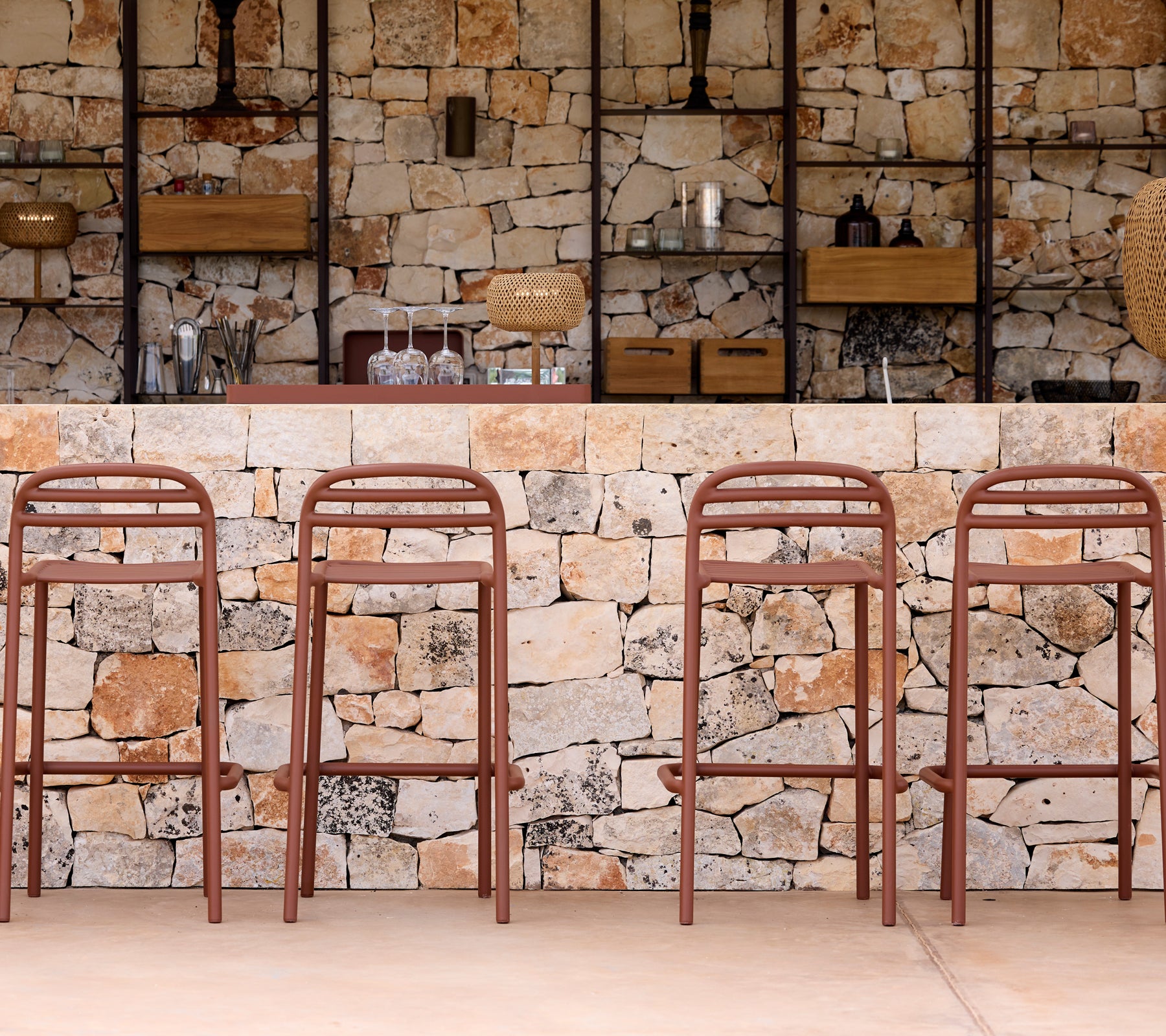 Brown bar stools in front of a stone wall with shelves.