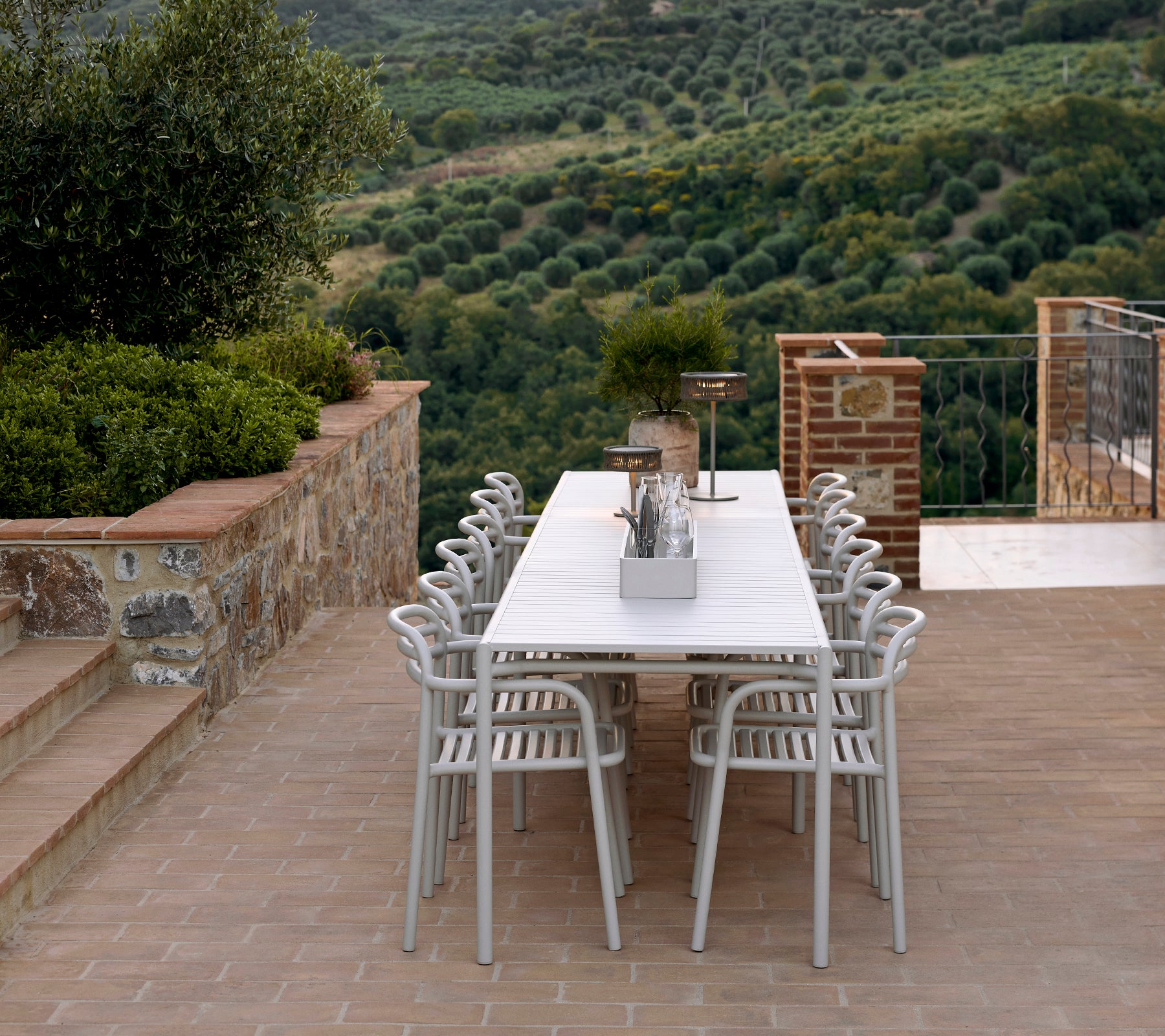 A stylish seating arrangement featuring Bliss chairs and table in sand color, complemented by an Illusion lamp, set against a lush landscape.