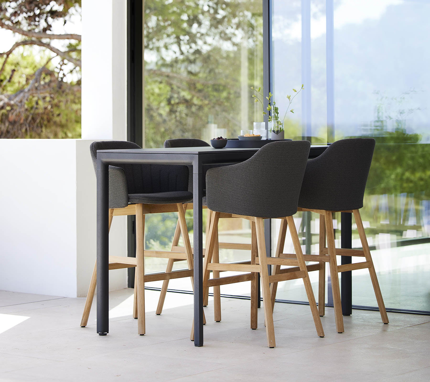 A stylish drop bar table accompanied by four modern bar chairs with wooden legs and upholstered seats.