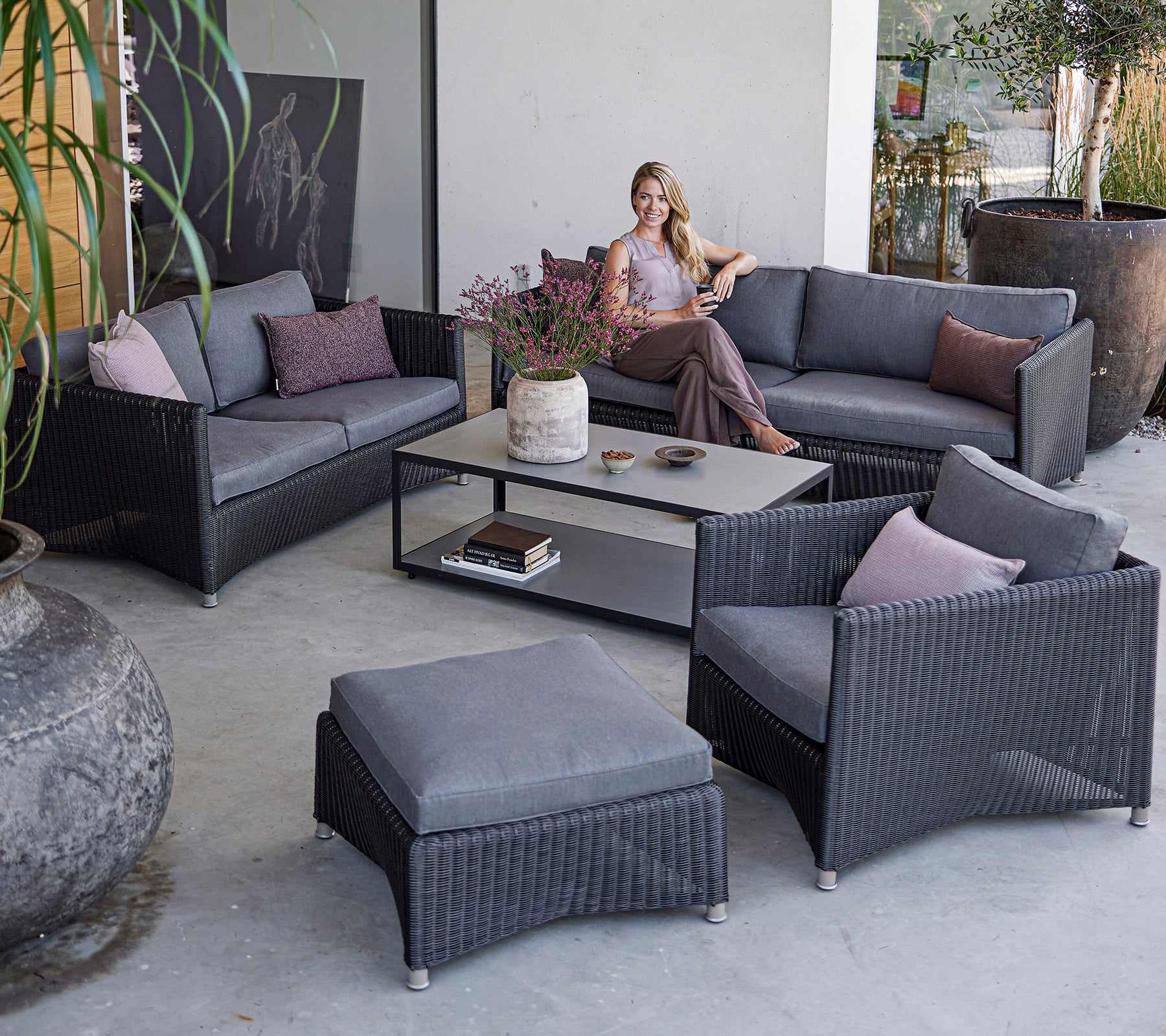 A modern outdoor seating arrangement featuring a woman relaxing on a stylish gray fabric sofa set with cushions and a coffee table.