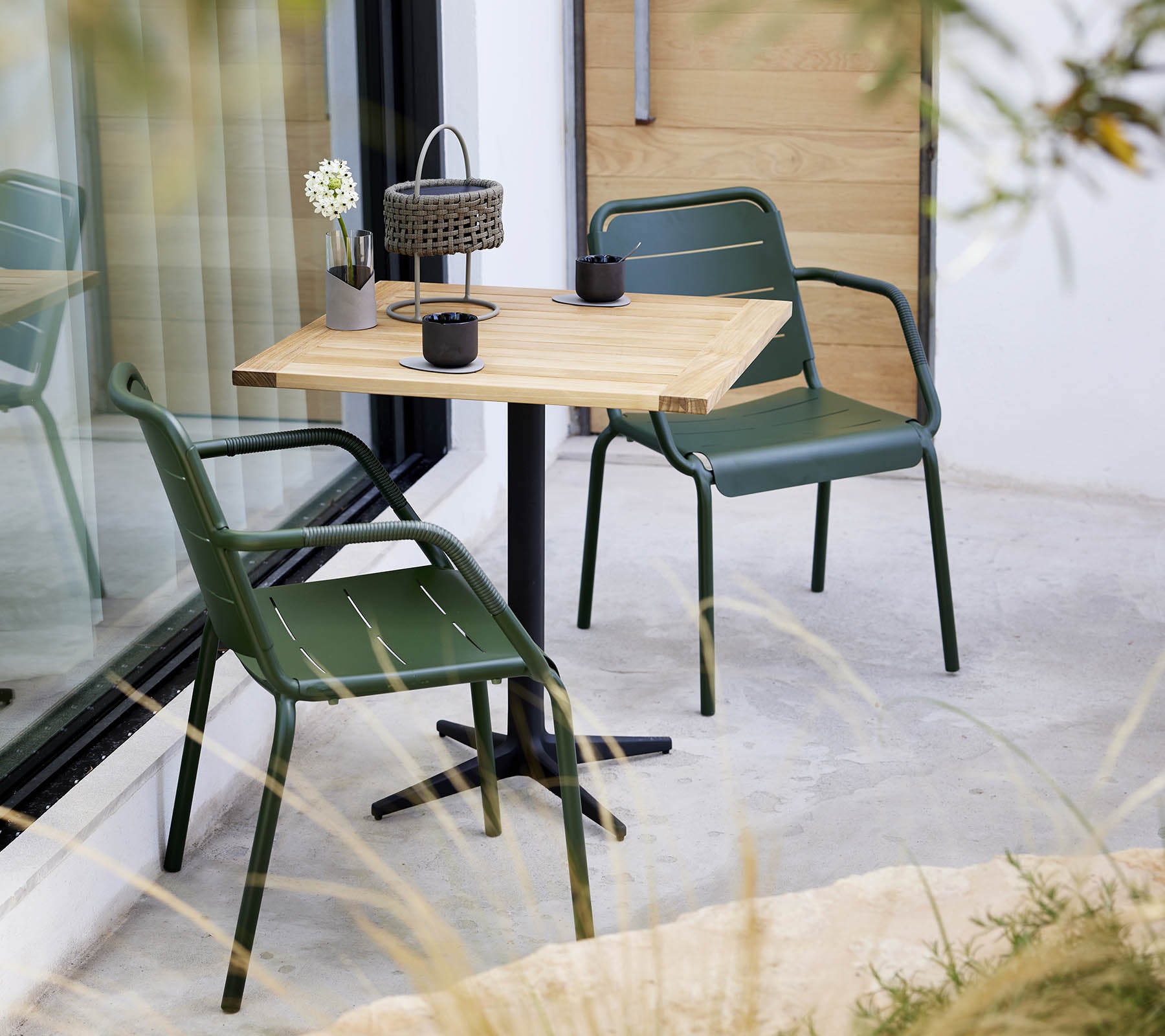 A minimalistic setting with a wooden table and green chairs, featuring a small flower arrangement and decorative lantern.