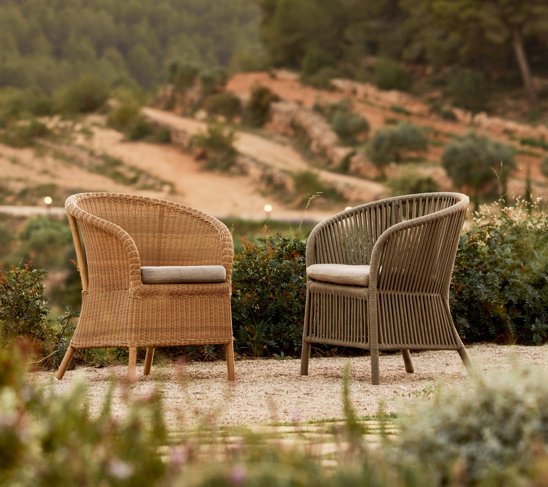 Two stylish Derby chairs in contrasting colors, set among greenery with a scenic backdrop.