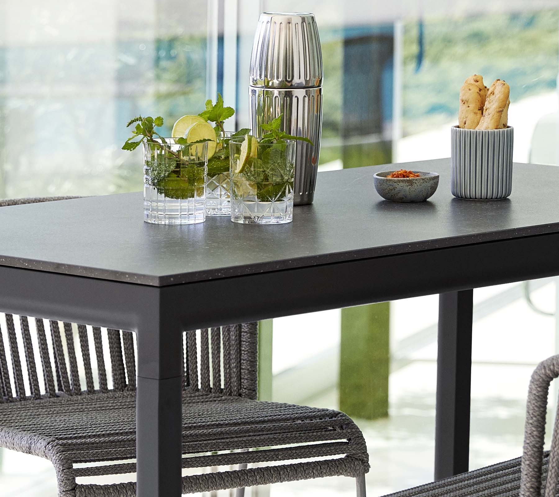 A modern table set with plants in glass vases, a decorative container, and a dish of snacks, surrounded by stylish chairs.