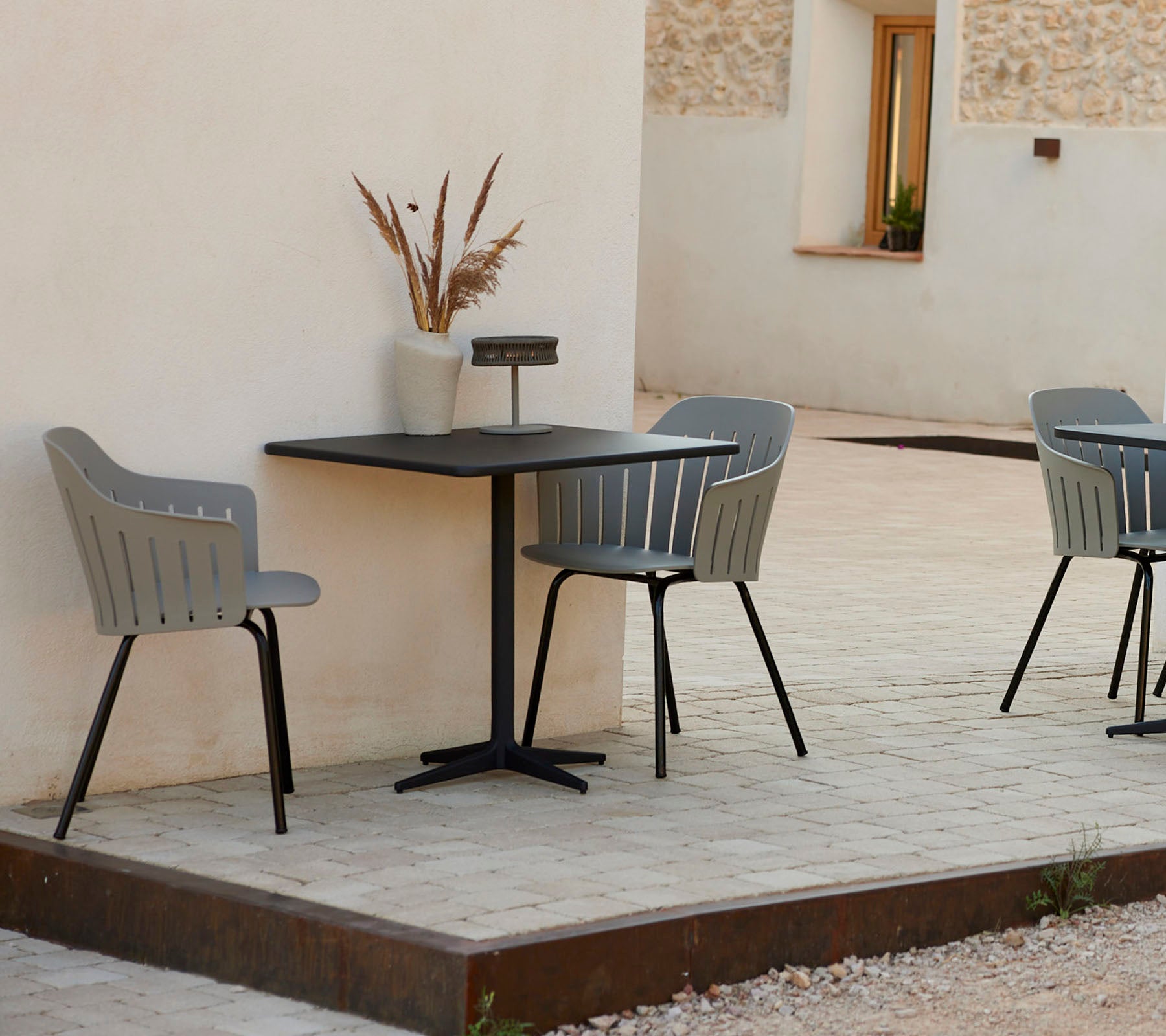 A modern café table with two stylish gray chairs, accompanied by a decorative vase, set against a simple backdrop.