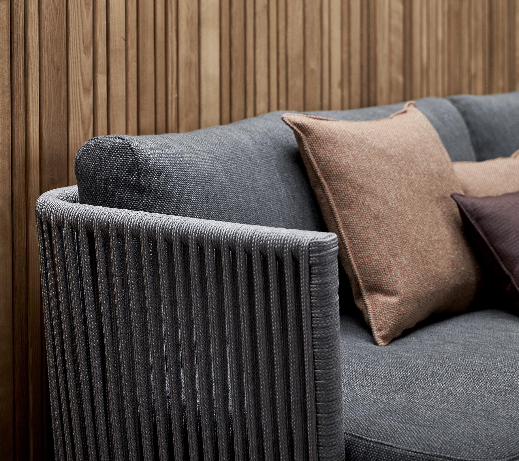 Stylish sofa featuring a textured gray fabric with decorative pillows in earthy tones and a vertical striped armrest design.