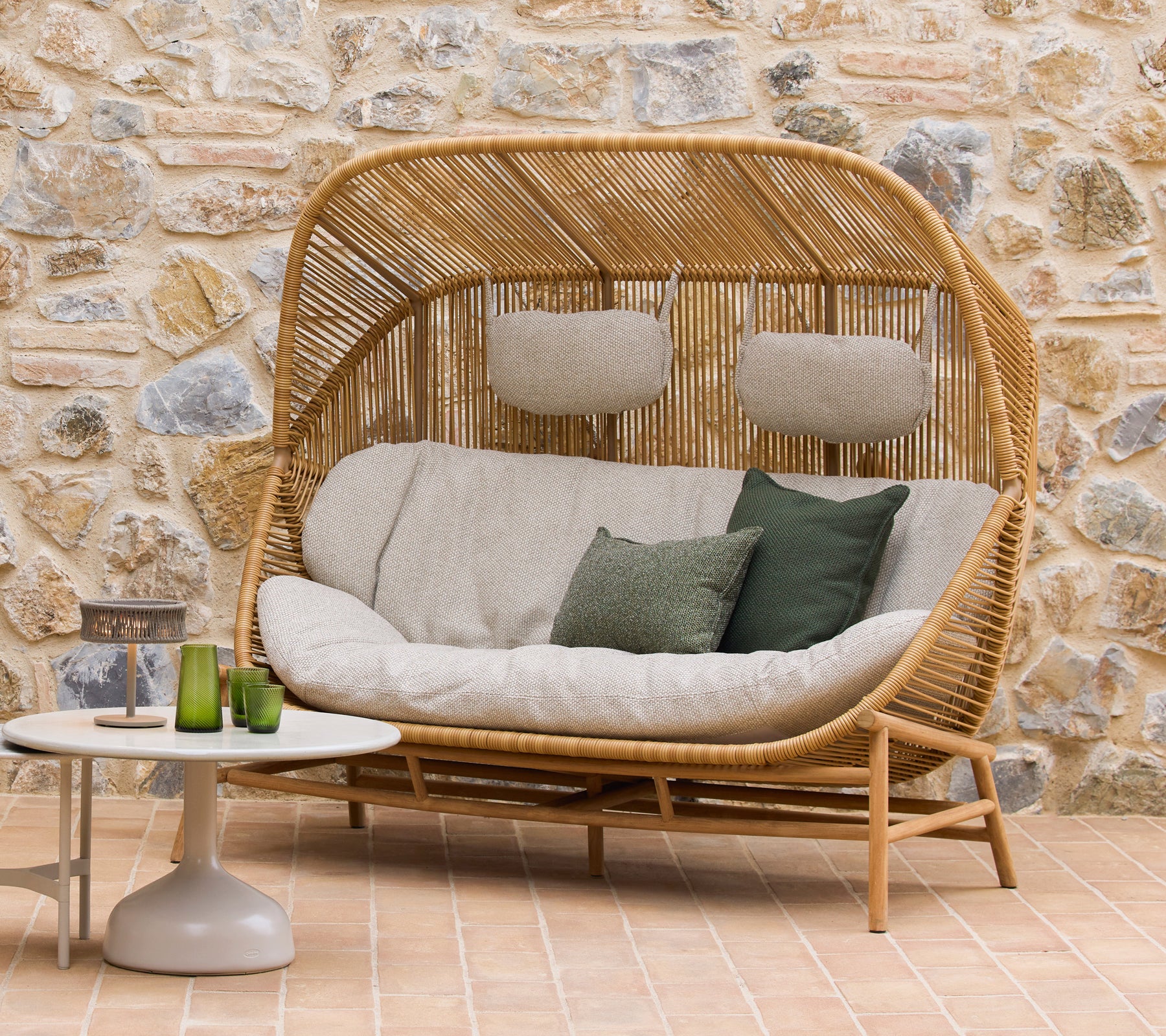 Hive sofa with plush cushions and green accents alongside Glaze coffee tables, set against a natural stone backdrop.