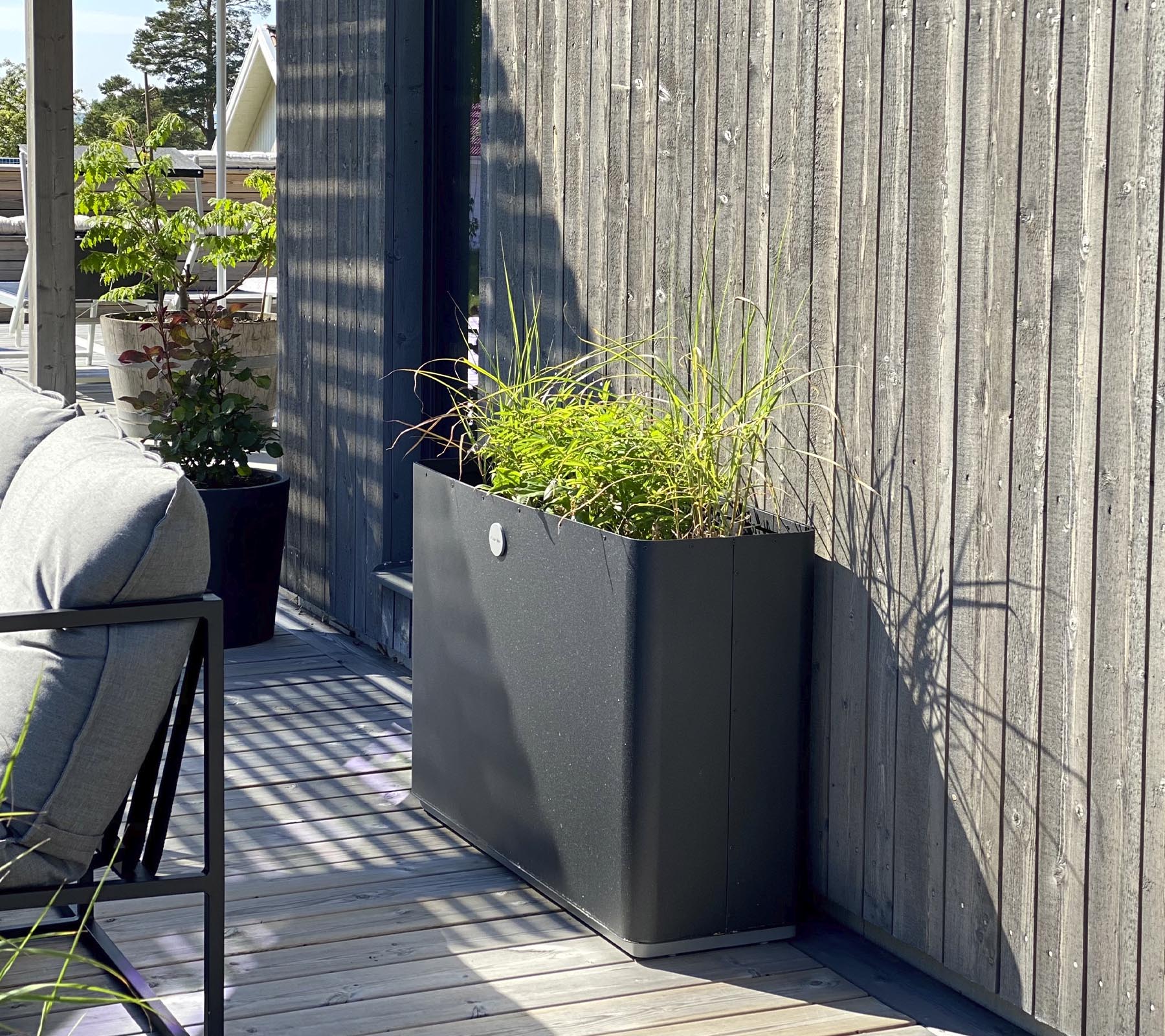 A sleek, modern planter with vibrant greenery sits against a textured wooden wall, complementing the surrounding space.