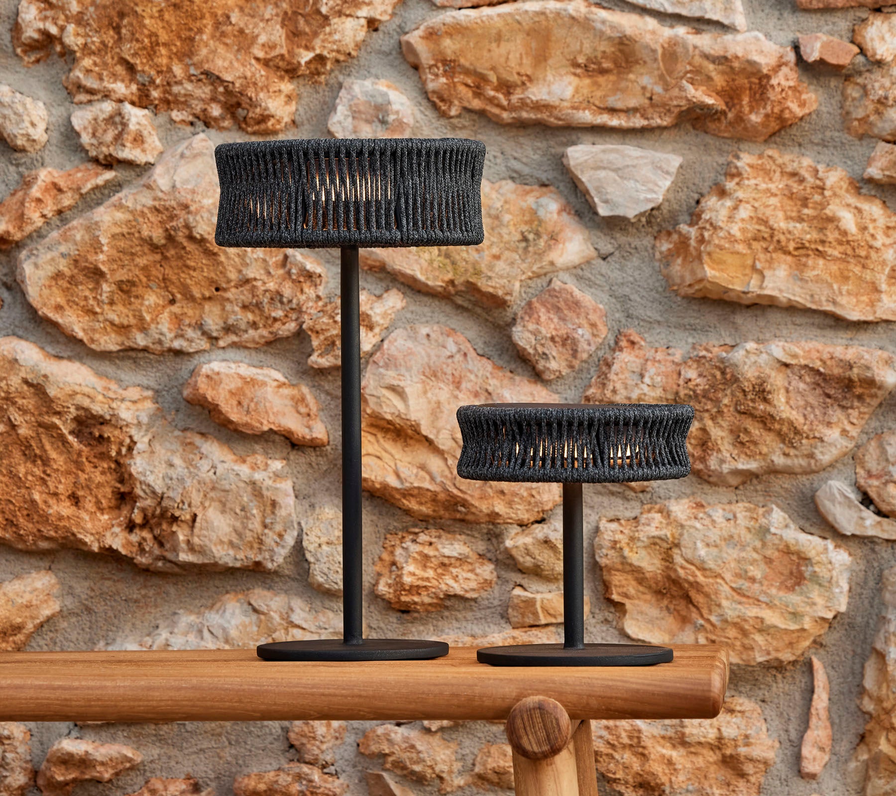 Two stylish table lamps with a woven design, set against a textured stone wall, creating an elegant and inviting atmosphere.