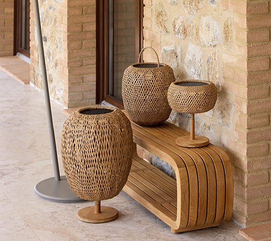 Three woven glow lamps in varying heights arranged on a wooden bench, complemented by a sleek stand. Natural materials create an inviting ambiance.