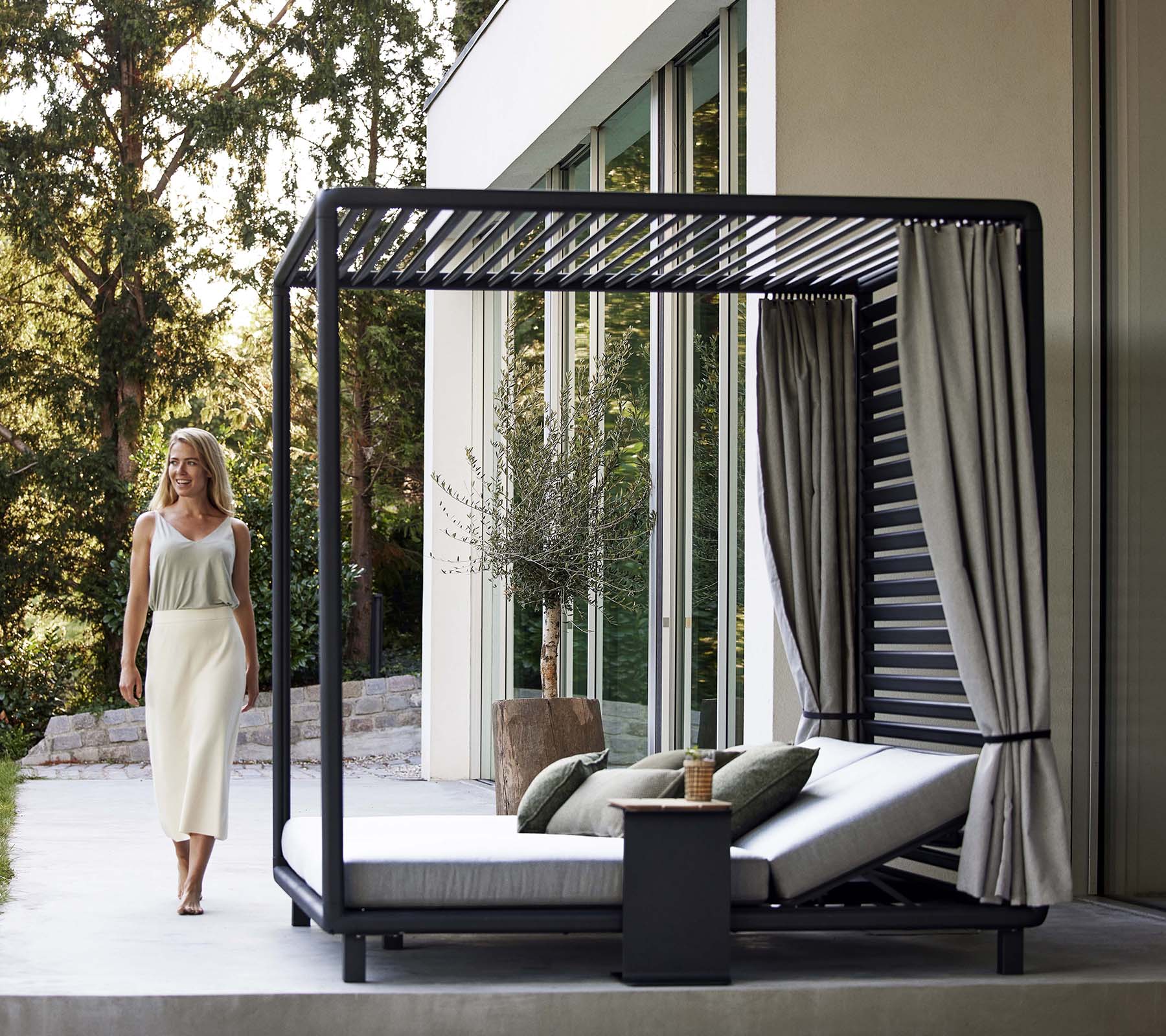 A stylish cabana featuring a sleek design with soft cushions, curtains, and a small side table, set in a serene, natural environment.