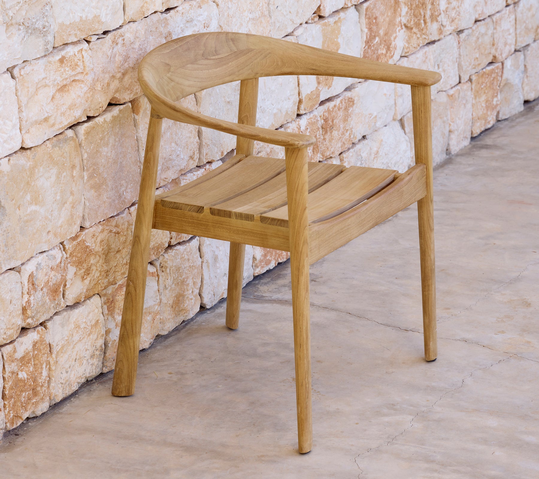 Modern wooden chair beside a stone wall in a minimalist setting.