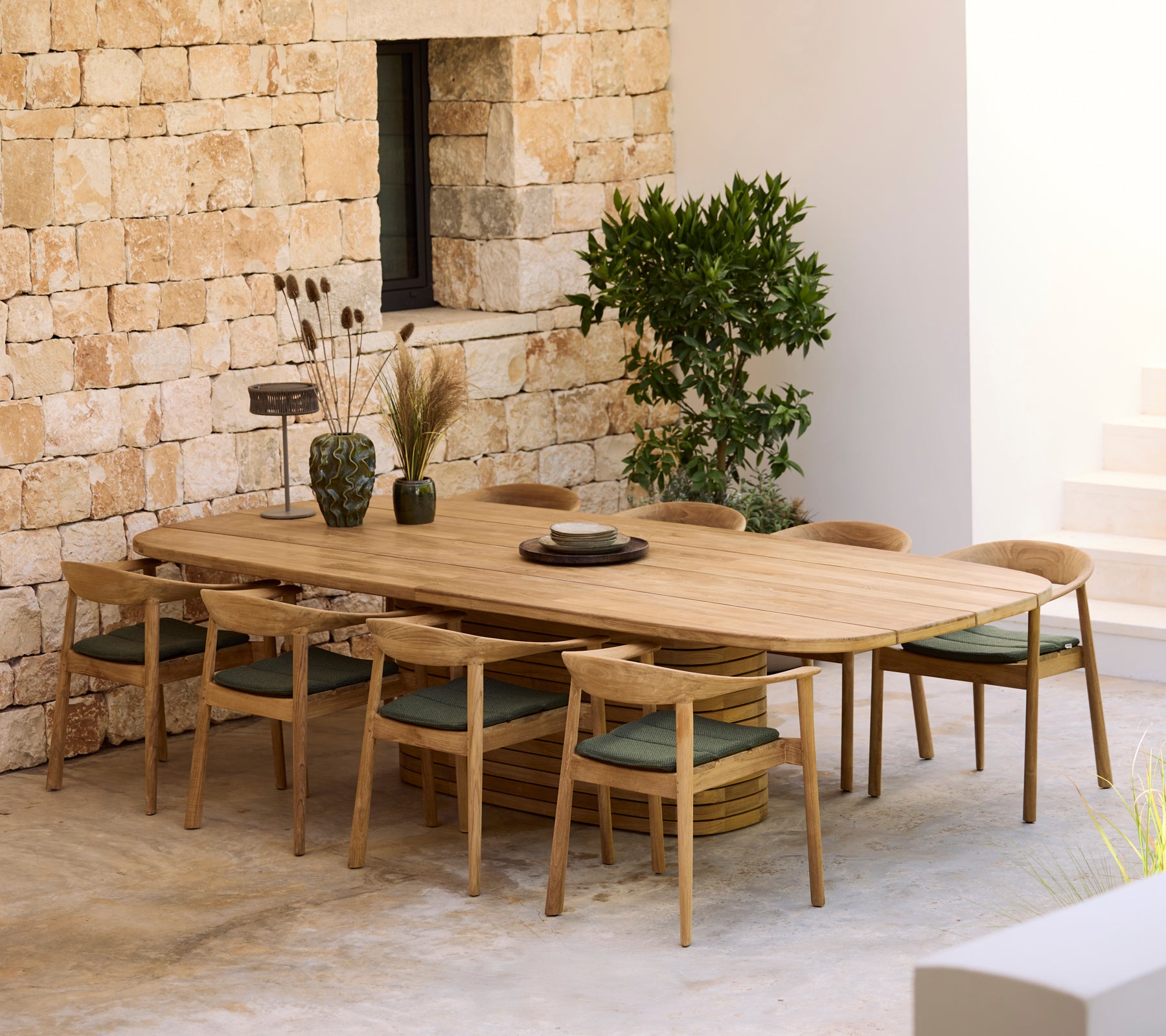 Modern wooden dining table with green cushions and wooden chairs in a minimalist setting.