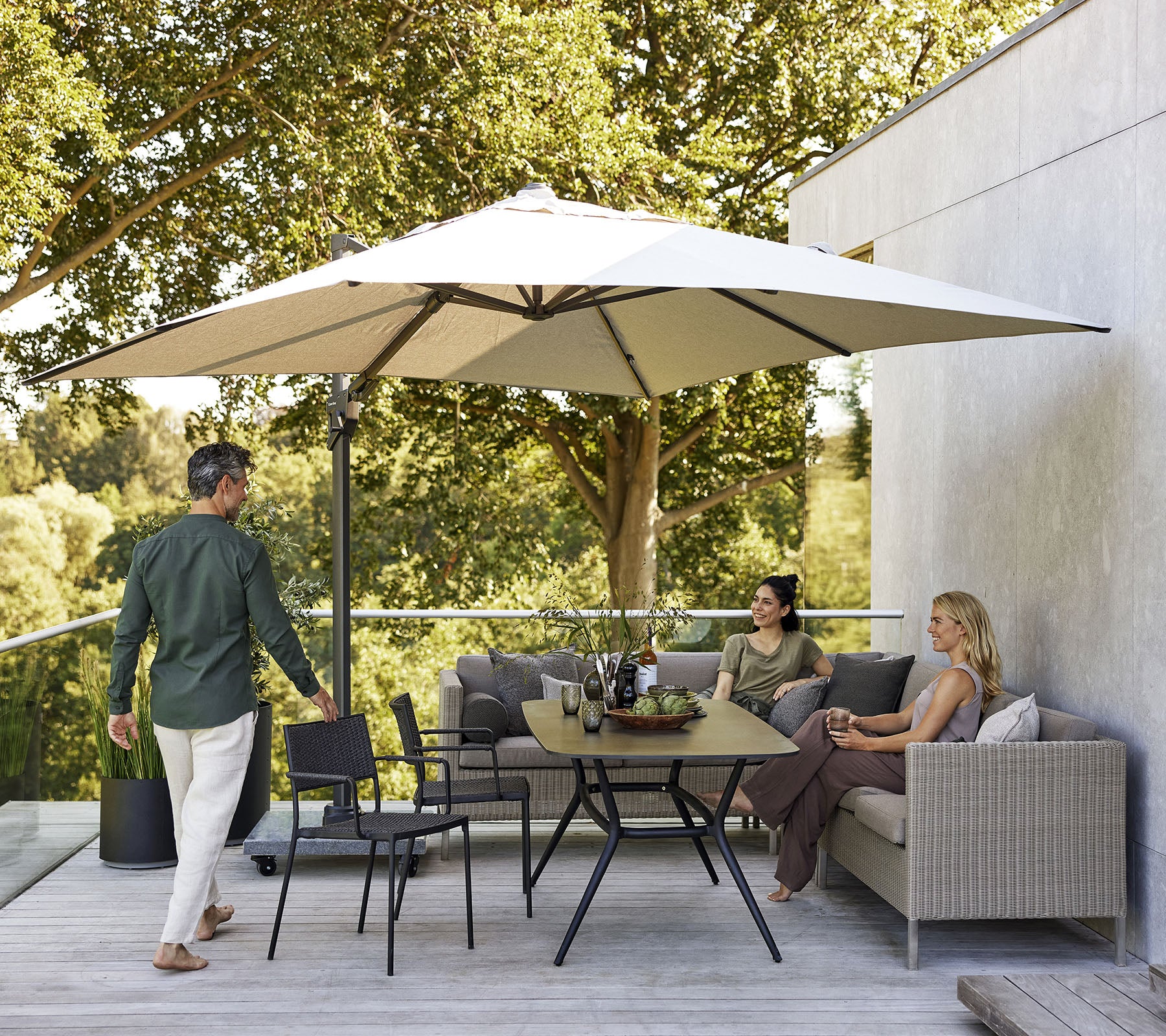 A stylish seating area with a large umbrella, featuring a sofa, chairs, and a dining table surrounded by lush greenery.