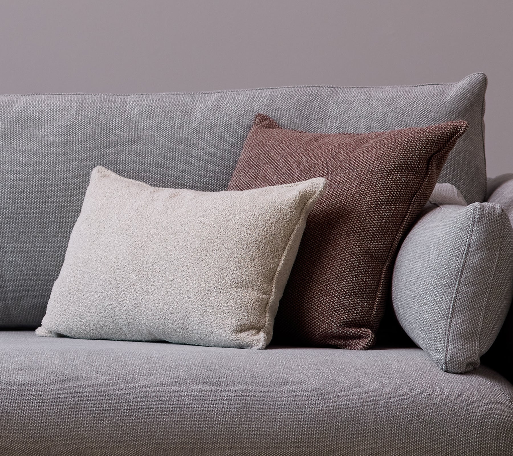 A white Scent scatter cushion and a Wove dark bordeaux cushion are placed on a gray sofa.