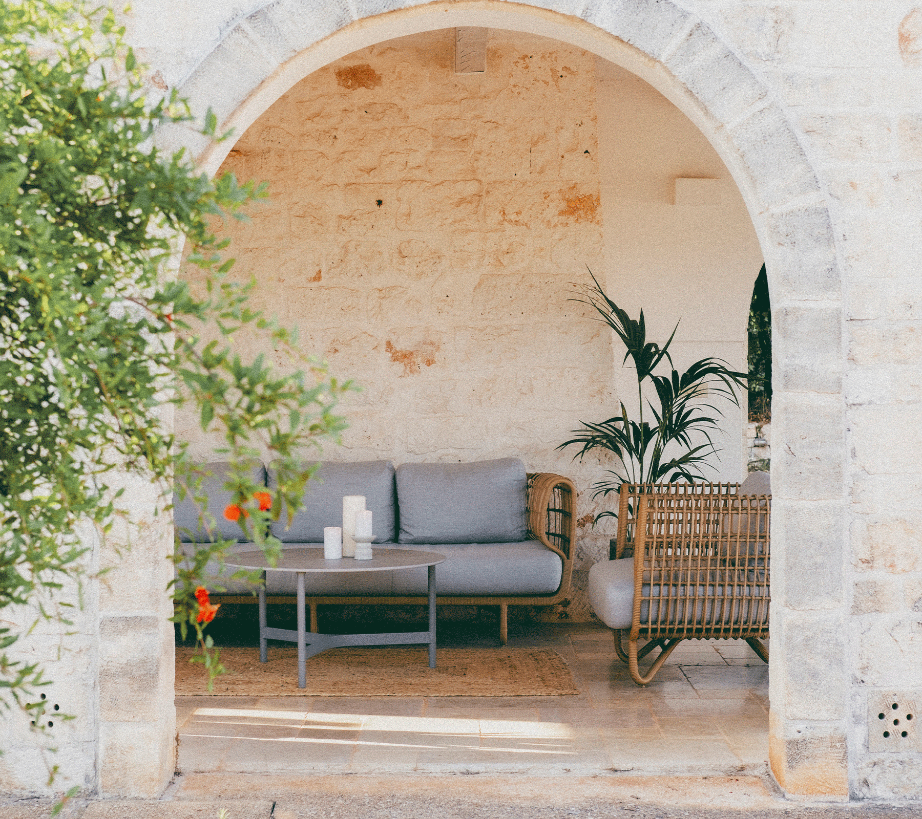 Cozy seating area framed by an arch, featuring a sofa, coffee table, plants, and decorative elements.